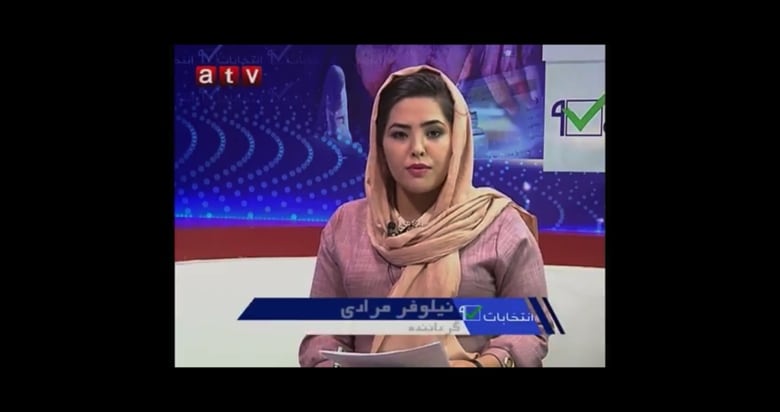 A still of a TV news report. A woman holds a script and looks directly at the camera. 