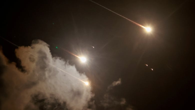 Explosions and the streaks of missiles are seen against a nighttime sky.