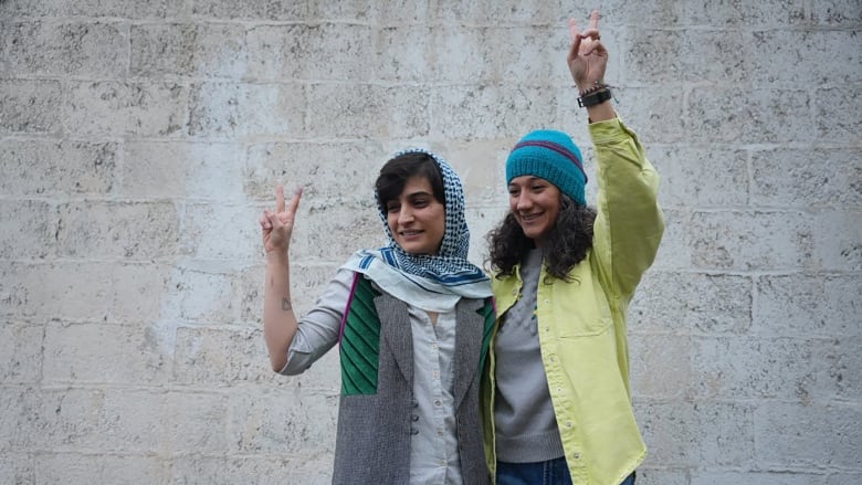 Two young women smile and flash peace signs