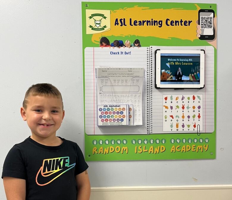 A young boy is standing next to a cardboard that says 