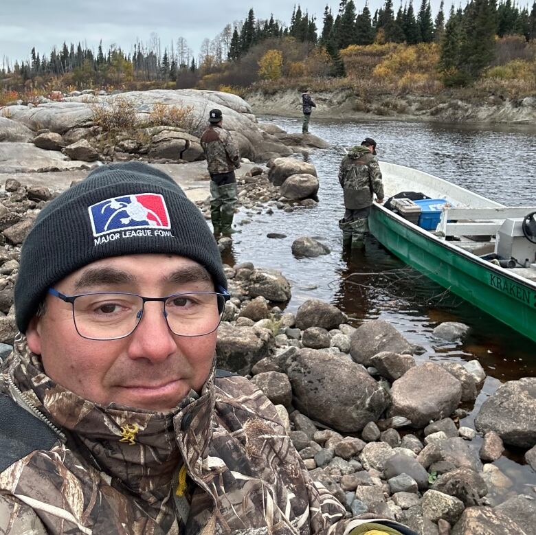 A man looking over a lake, men are shoring a boat. 