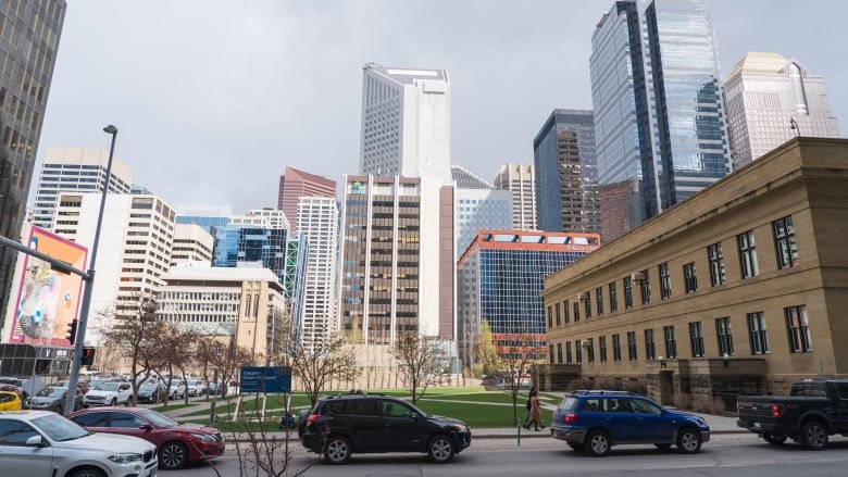 a road with many vehicles is in the foreground of an image of multiple buildings. two people walk on a city street.