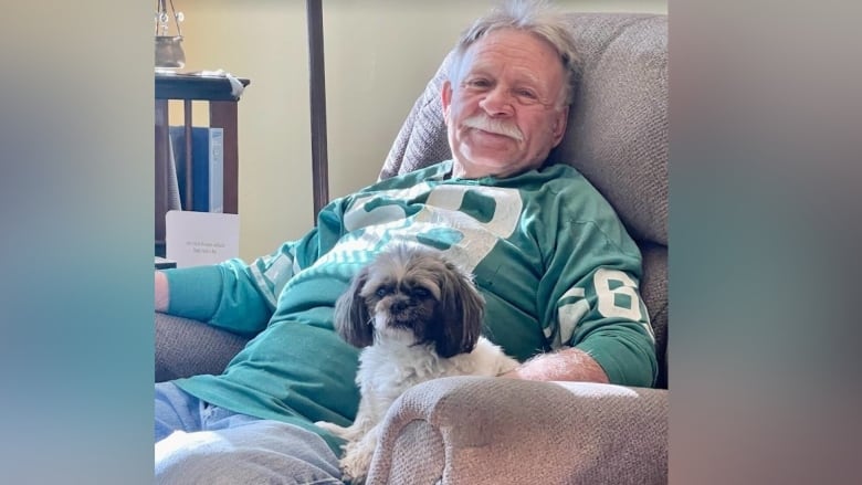 A man sits in an armchair with a dog. 