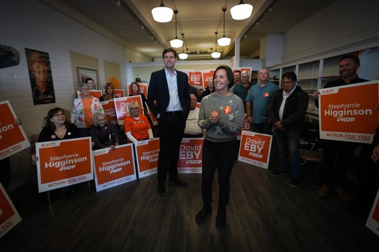 A group of people in a room full of orange NDP signs.