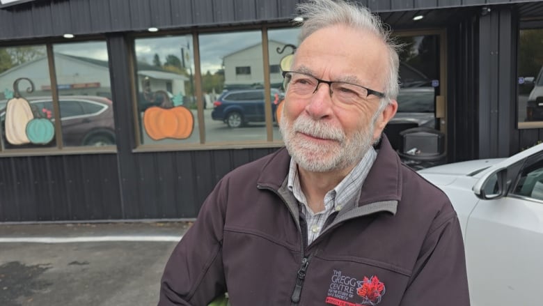 A man with grey hair and a beard outside a store with pumpkins painted on the windows.