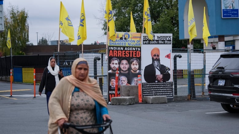 A poster with a man's face is pictured behind a woman walking down a street.