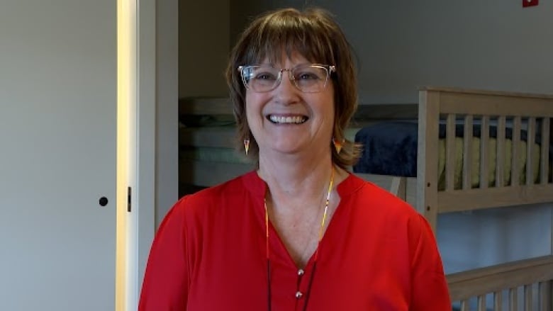 A woman with short blonde hair smiles. She is wearing a red shirt.