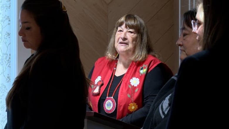 A woman in a red vest speaks at a podium.