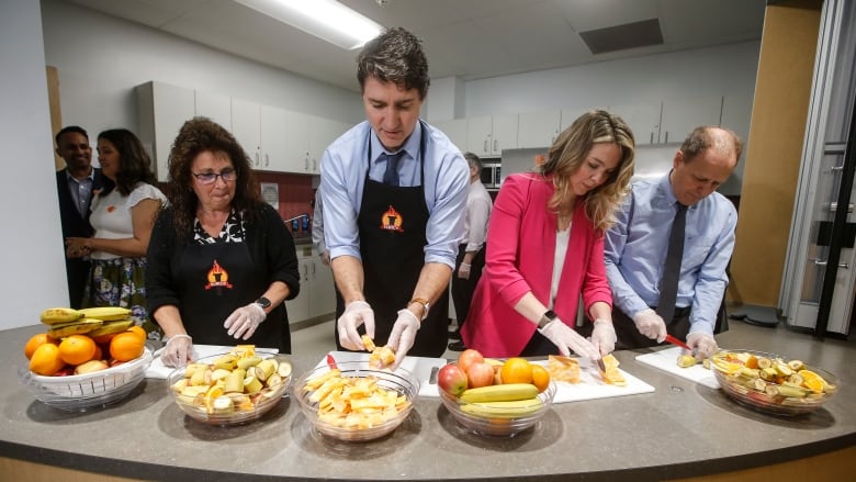 Educational assistant Kim Jemielity (left) cuts up fruit for students while wearing disposible gloves at a counter alongside Prime Minister Justin Trudeau, Social Development Minister Jenna Sudds and Liberal MP Kevin Lamoureux at Elwick Community School in Winnipeg on May 17. 