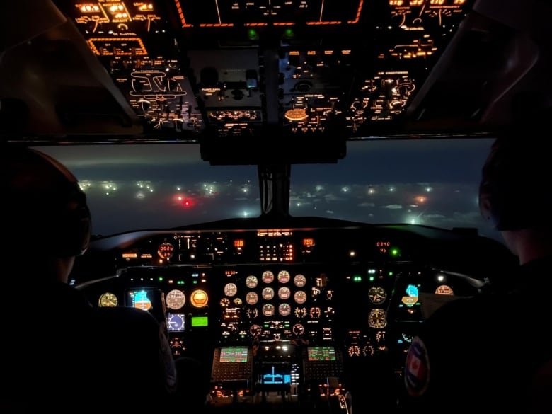 The cockpit of a Dash-8 plane flying over the lights from fishing vessels in the North Pacific.