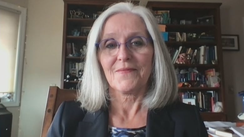 A woman with glasses and long white hair looks into a Zoom screen from her book-lined office. 