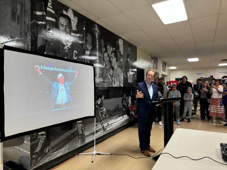 A man speaks at a podium in front of a large mural