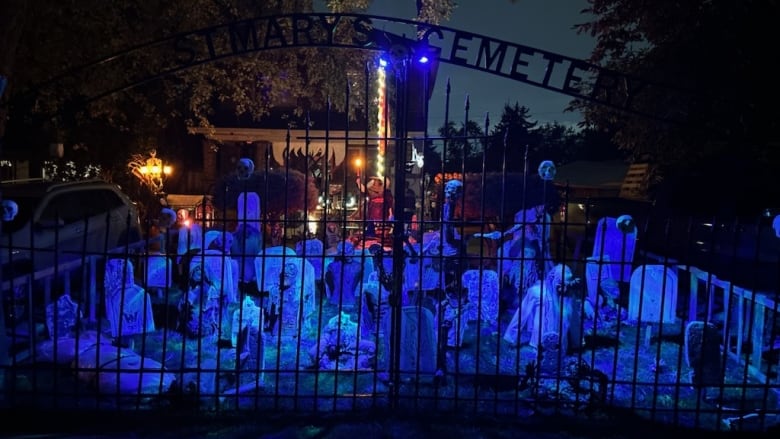 A fenced area lit with a black light filled with glowing tombstones and ghosts. 