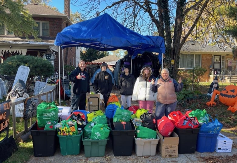 Several people standing with 15 or 20 rubber bins and grocery backs full of clothing and groceries. 