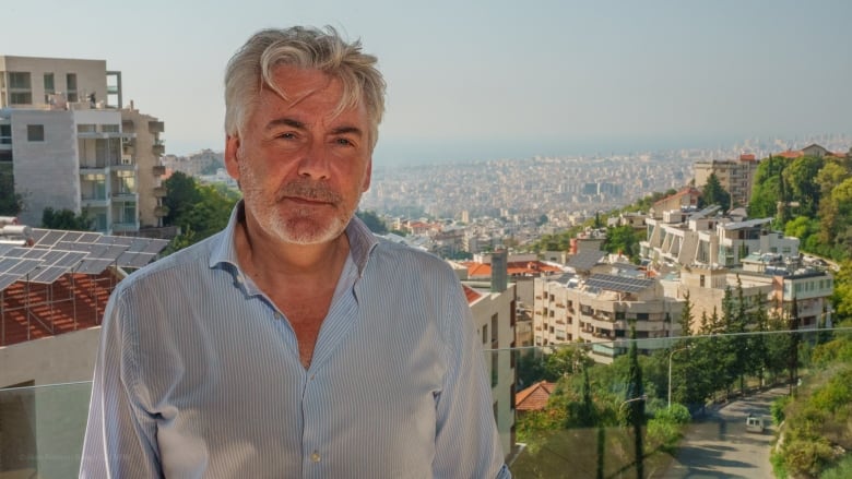 A man in a dress shirt poses for a photo. A Mediterranean city is in the background. 