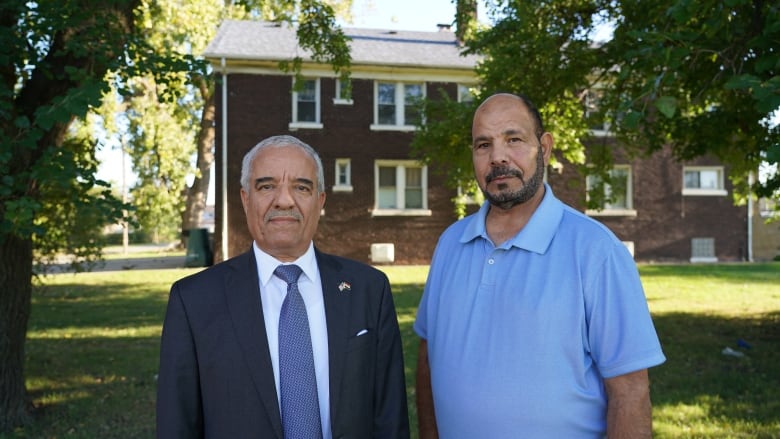 Two men, one in a suit and tie and one in a blue polo shirt, stand together for a photo.