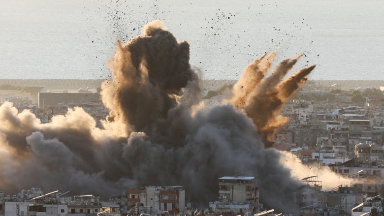 Dust, smoke and debris erupt from a dense urban centre following an airstrike.