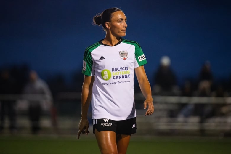 A women's soccer player is shown walking on the pitch.