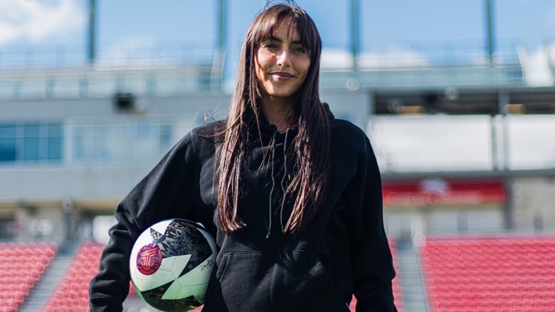 A woman holds a soccer ball while staning on the pitch.