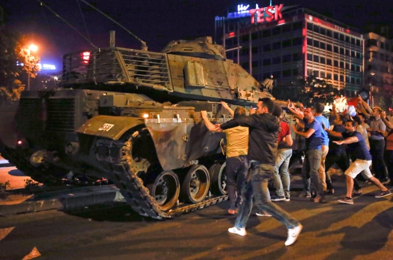 Several woman are shown standing near a tank in the streets.