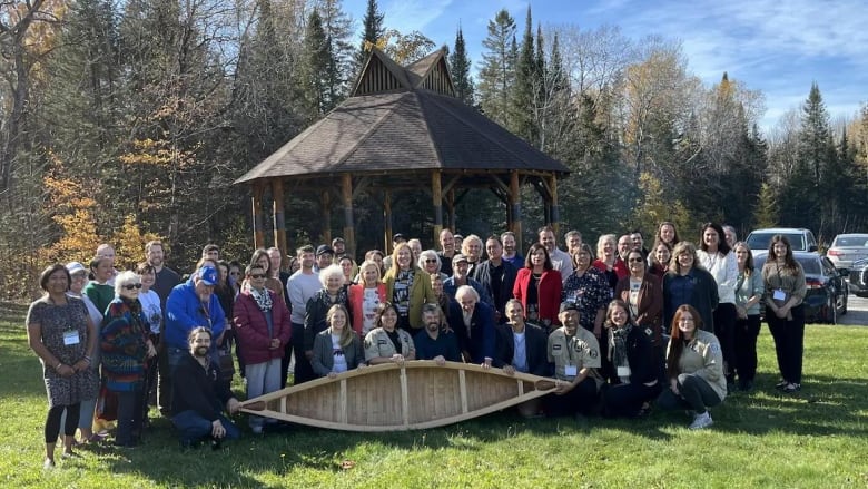 A crowd of people pose for a group picture. A few in the front are holding a wooden canoe.