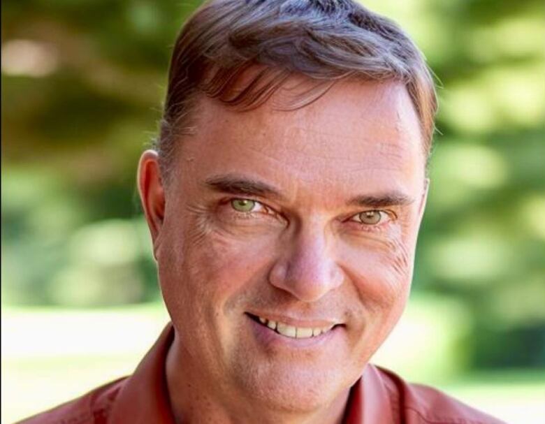 Headshot of a man with blurred green nature in the background.