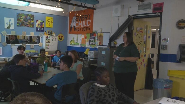 A teacher stands talking to a class full of students.