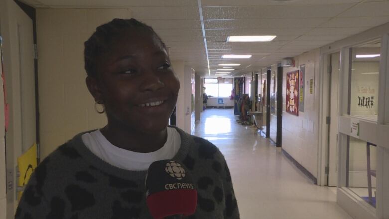 A young Black girl speaks in a hallway with lockers.