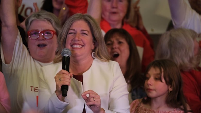 A woman holds a microphone and smiles.