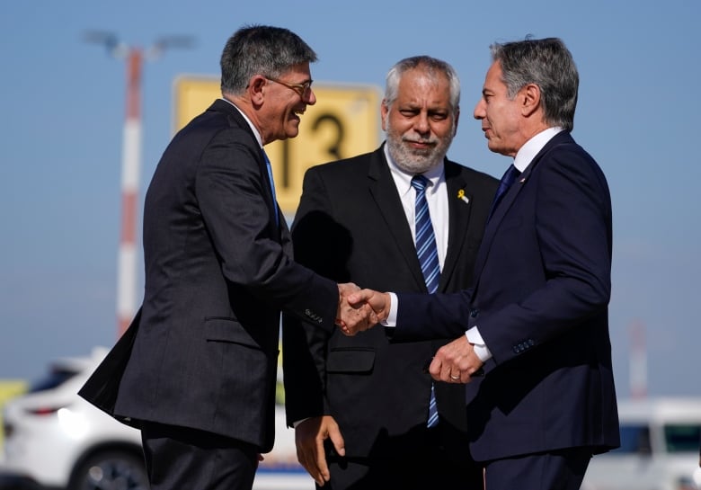 Three men in suits greet each other on a  tarmac