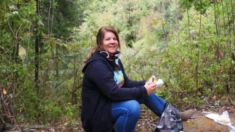 A woman sits among trees, smiling at the camera.