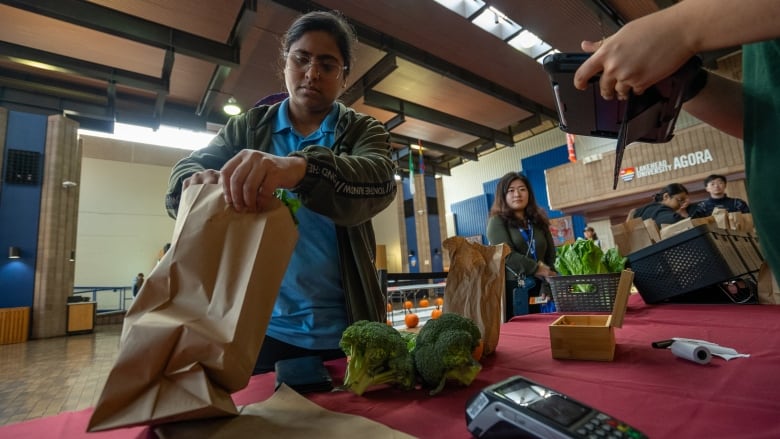 A person is seen putting produce into a brown paper shopping bag.