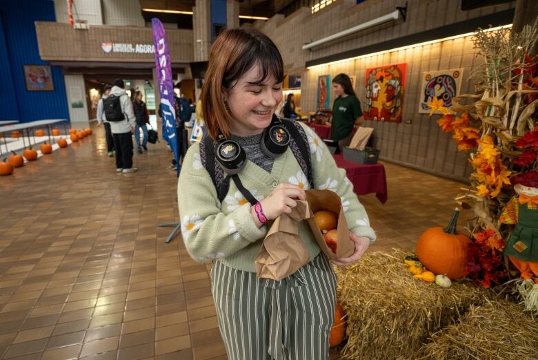 A person holds a paper shopping bag open. They are standing next to bales of hay inside a building.