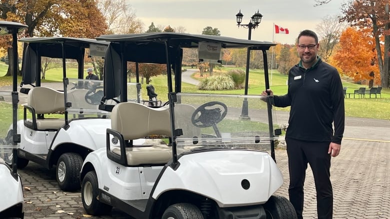 A man stands beside a golf cart. 