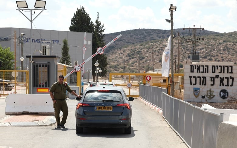 A soldier leans against a car waiting at a checkpoint.