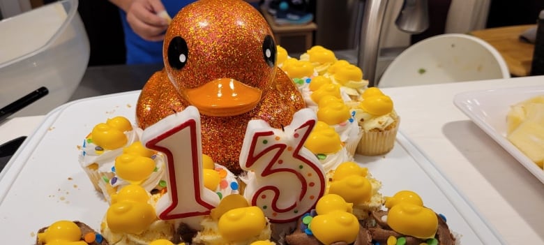 A giant sparkly duck decoration sits amidst smaller yellow ducks, with a 13th birthday candle sitting in the middle.