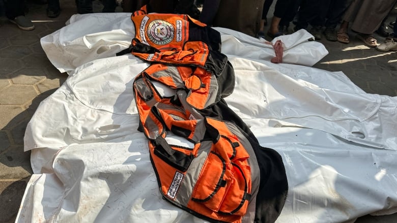 White body bags with orange vests on top