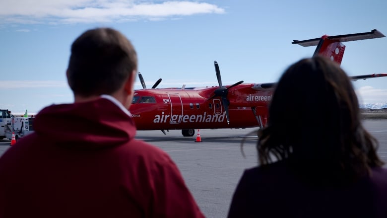 the backs of two people with a plane in the background