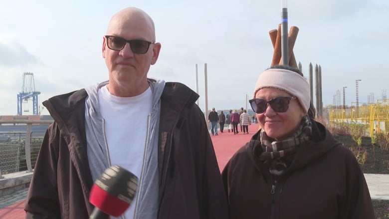 Man and a woman standing side by side speaking to camera. 