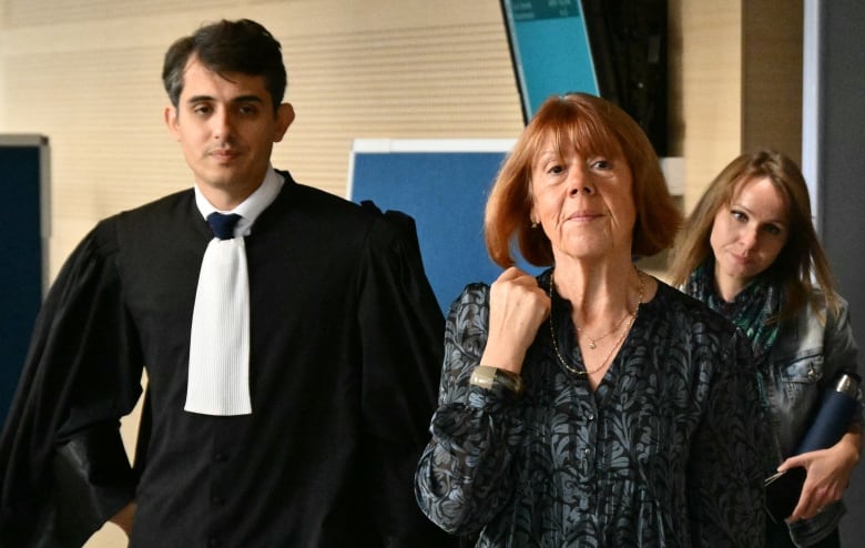 A woman walks into a crowded courthouse flanked by a lawyer