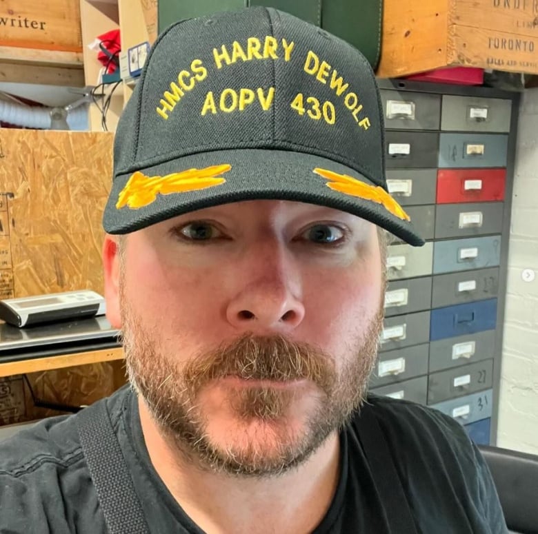 A man is seen wearing a HMCS Harry DEWolf baseball cap.