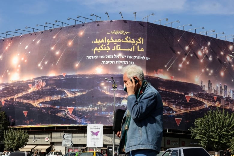 A man holding a phone walks past an anti-Israel billboard in Tehran. 