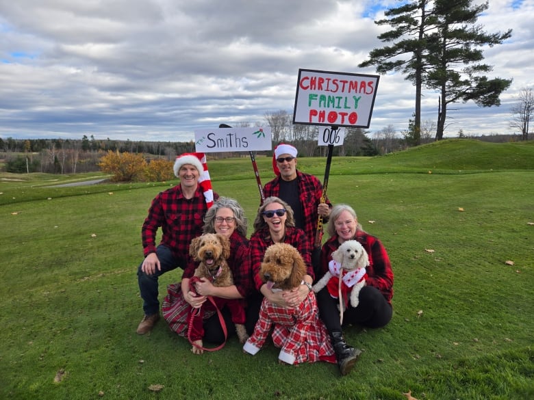 A group of people wearing red plaid, with three dogs in the foreground dressed in red and white and green.