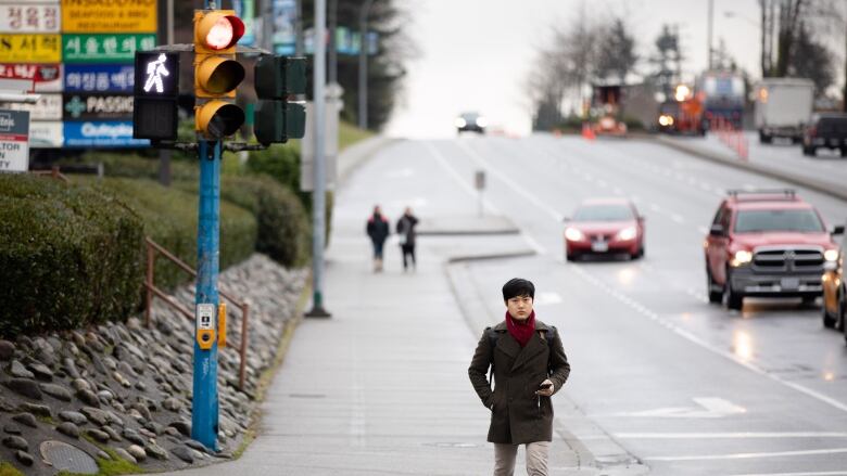 A person crosses an intersection with cars behind them on a cloudy day.