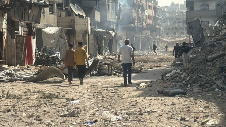 People walk past damaged and destroyed buildings.