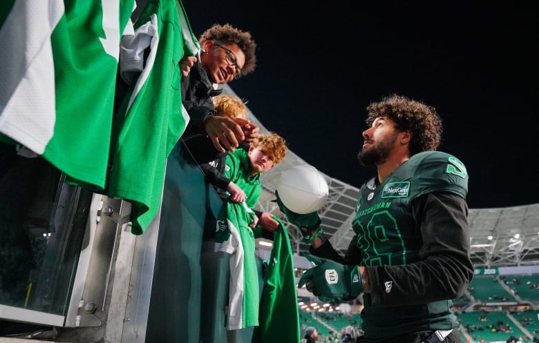 A football player hands a football to a young fan in the stands.