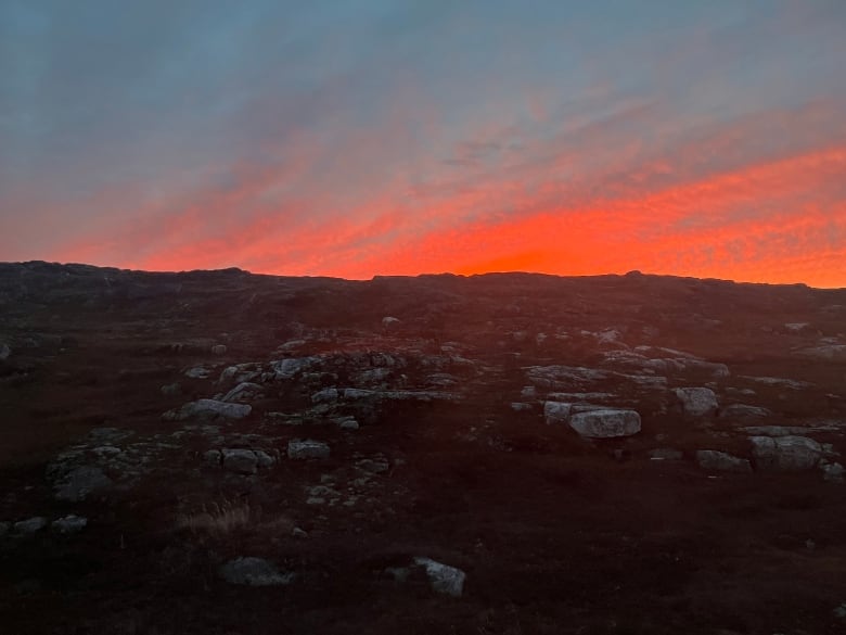 A rocky terrain with a sky lit up with pinks and blues.