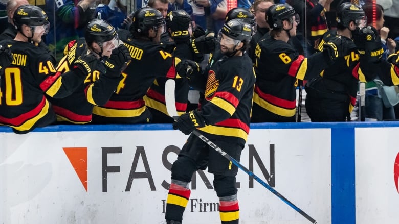 A hockey player smiles as his teammates give him high fives along the bench.