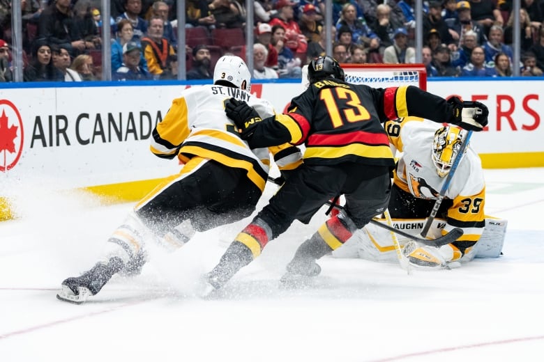 Two hockey players go for the puck as a goalie makes a save.