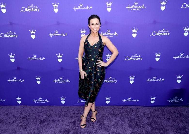 A woman in a dress poses in front of a purple background  that says 'hallmark'